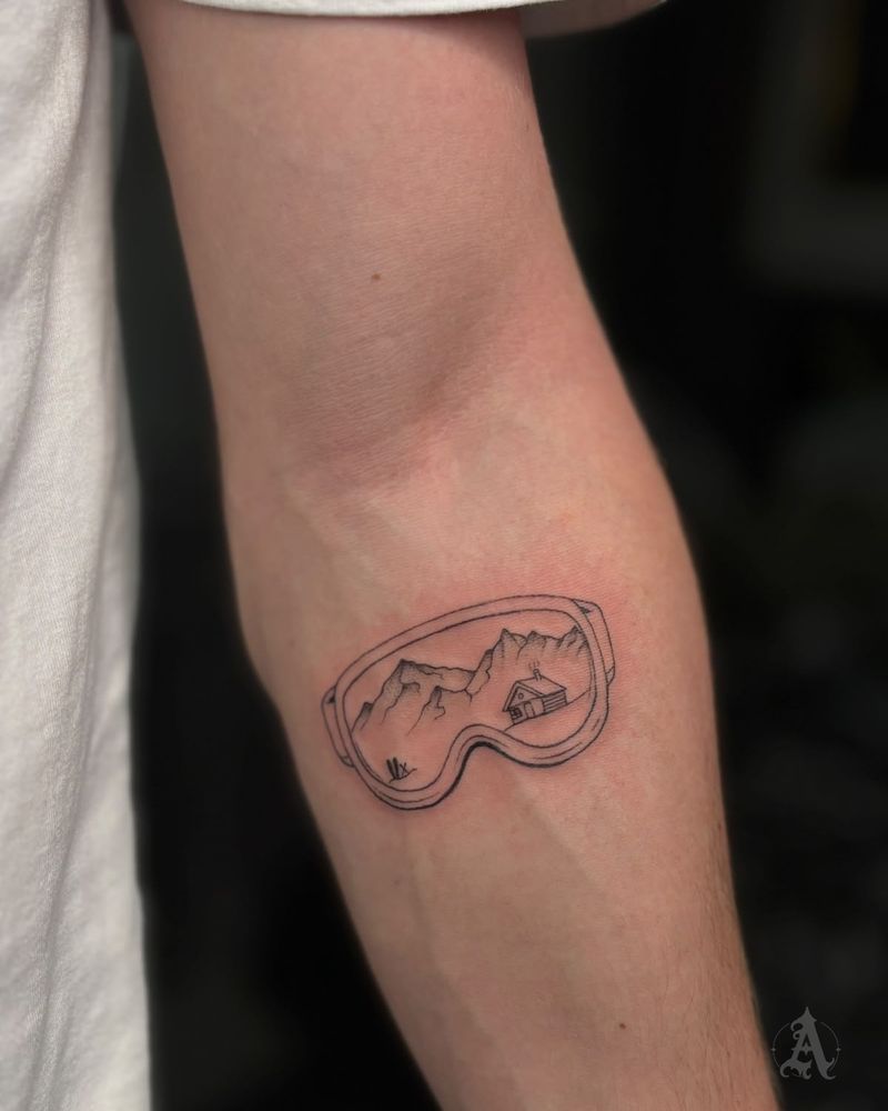 Tatuaje de paisaje montañoso dentro de gafas de nieve en el brazo, fine line en negro y gris