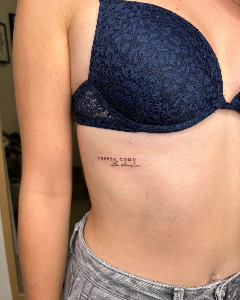 Tatuaje de frase bajo el pecho en el costado, fine line en negro y gris