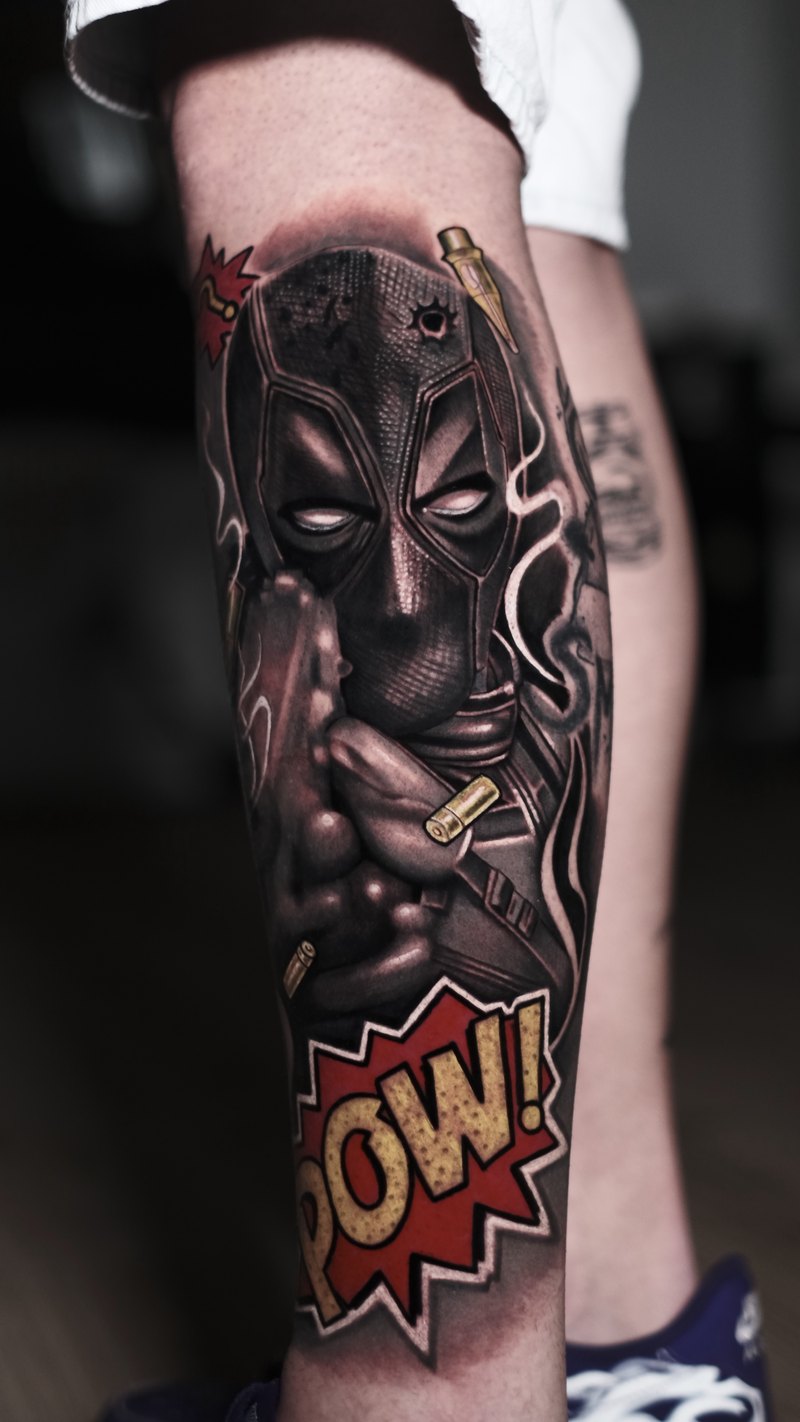 Tatuaje realista de Deadpool a color en la pierna, con casquillos y un POW! de cómic