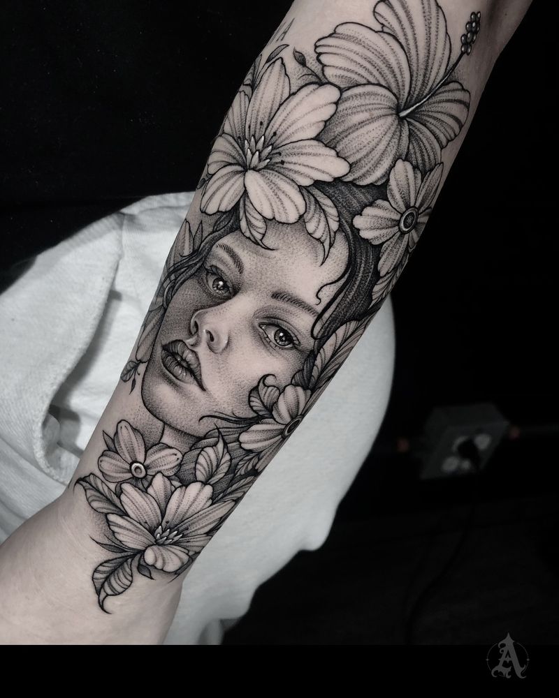 Tatuaje de retrato femenino entre flores en antebrazo, realismo en negro y gris